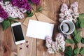 Bouquet of lilac flowers on wooden planks with blank card for text , gift, coffee and mobile phone. Top view