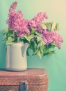 Bouquet of lilac in an old enameled teapot on vintage suitcase on blue background. Retro style still life.