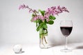 Bouquet of lilac in a vase, a glass of wine and a transparent ball