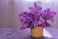Bouquet of lilacs in a basket on a table against a window background. Copy space.