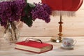 Bouquet of lilacs, book, spectacles, cup of tea and table lamp