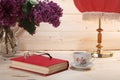 Bouquet of lilacs, book, spectacles, cup of tea and table lamp