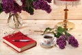 Bouquet of lilacs, book, spectacles, cup of tea and table lamp