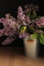 A bouquet of lilacs in a bucket on a wooden table. Spring. Still life in a low key.