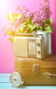 Bouquet of lilacs in enameled kettle on antique suitcase, vintage radio, alarm clock on pink background. Retro style still life.