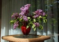 Bouquet of lilacs in a glass vase standing on a small wicker table Royalty Free Stock Photo