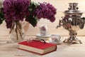 Bouquet of lilacs, samovar, cup of tea, book and spectacles Royalty Free Stock Photo