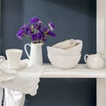 A bouquet of limonium and a set of white dishes: porcelain milk jug, coffee cup, bowls on a white rack on a dark blue background Royalty Free Stock Photo