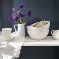 A bouquet of limonium and a set of white dishes: porcelain milk jug, coffee cup, bowls on a white rack on a dark blue background Royalty Free Stock Photo