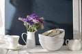 A bouquet of limonium and a set of white dishes: porcelain milk jug, coffee cup, bowls on a white rack on a dark blue background Royalty Free Stock Photo