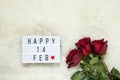 Bouquet of maroon roses on milk white fur carpet, lightbox with inscription Happy 14 FEB that means Valentine`s Day. Flat lay. To