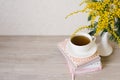 A bouquet of mimosa in a white vase, a cup of tea on a stack of notebooks for notes Royalty Free Stock Photo