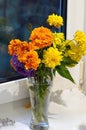 Bouquet of orange marigolds, blue aster and yellow flowers in a glass vase. The bouquet stands on a white window sill Royalty Free Stock Photo