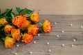 Bouquet of orange roses on wooden background and scattered beads of pearls. The best present on holiday.