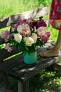 Bouquet of peony flowers in milk can, woamn standing on wooden garden bench Royalty Free Stock Photo