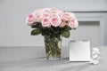 A bouquet of pink double roses in a glass transparent vase on a table covered with a gray tablecloth. Notebook. And a statuette of