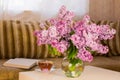 Bouquet of pink lilacs in a vase on a book table.