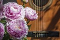 Bouquet of pink peonies is near brown guitar