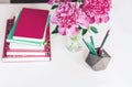 Bouquet of pink peonies, a stack of books, pencils and a notebook on a white table, top view Royalty Free Stock Photo