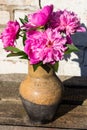 Bouquet of pink peony flowers in clay jug on rustic wooden table Royalty Free Stock Photo