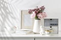 Bouquet of pink Persian buttercups on white table in front of a chest of drawers. Scandinavian style. Place for text