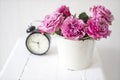 A bouquet of pink roses in a tin white bucket on an old stool with an alarm clock and a napkin with embroidery near the bed on a Royalty Free Stock Photo