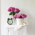 Bouquet of pink roses in a tin white bucket on an old stool with an alarm clock and a napkin with embroidery near the bed on a Royalty Free Stock Photo