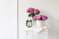 Bouquet of pink roses in a tin white bucket on an old stool with an alarm clock and a napkin with embroidery near the bed on a Royalty Free Stock Photo