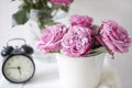 A bouquet of pink roses in a tin white bucket on an old stool with an alarm clock and a napkin with embroidery near the bed on a Royalty Free Stock Photo