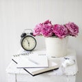 A bouquet of pink roses in a tin white bucket on an old stool with an alarm clock and a napkin with embroidery near the bed on a Royalty Free Stock Photo