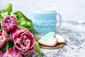 Bouquet of pink tulips, a cup of tea, and sweet gingerbread cookies in the shape of a heart on a light background. Copy space. Royalty Free Stock Photo