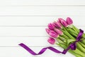 Bouquet of pink tulips decorated with purple ribbon on white wooden background. Royalty Free Stock Photo