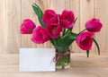 Bouquet pink tulips flowers in glass white vase with white paper card note with space for text on table on a wooden background Royalty Free Stock Photo