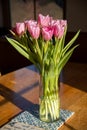 A bouquet of 10 pink tulips with fresh green leaves in a glass vase on a blue and white patterned tile and wooden table Royalty Free Stock Photo