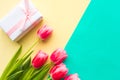 Bouquet of pink tulips and gift box on yellow and green background. Easter or Mother`s Day greeting card. Royalty Free Stock Photo