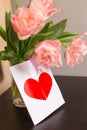 Bouquet of pink tulips in a glass vase with a postcard with a red heart. Romantic spring background with space for text. Royalty Free Stock Photo