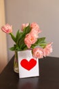 Bouquet of pink tulips in a glass vase with a postcard with a red heart. Romantic spring background with space for text. Royalty Free Stock Photo