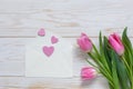 Bouquet of pink tulips and hearts pattern in paper envelope. Top view, close-up, flat lay on white wooden background Royalty Free Stock Photo