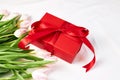 A bouquet of pink tulips and a red gift box on a beige bedspread. Gifts for the holidays. valentine's day