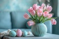 Bouquet of pink tulips in vase on table next to painted Easter eggs on blurred blue sofa background with daylight, interior of Royalty Free Stock Photo