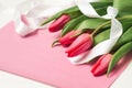 Bouquet of pink tulips with white decorative ribbon on rose lettering paper