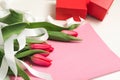 Bouquet of pink tulips with white decorative ribbon on rose lettering paper and red gift boxes
