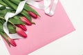 Bouquet of pink tulips with white decorative ribbon on rose lettering paper