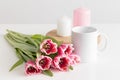 Bouquet of pink tulips, white mug and candles on a white table
