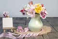 Bouquet from pink, yellow, magenta, white and red alstroemerias in pastel green vase with pink ribbon near small empty easel on