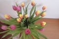 bouquet of pink and yellow tulips in vase top view across wooden drawer and whit wall. Interior decor. Royalty Free Stock Photo