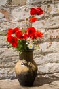 Bouquet of poppies and daisies in clay jug on wooden table against old brick wall Royalty Free Stock Photo