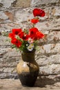 Bouquet of poppies and daisies in clay jug on wooden table against old brick wall Royalty Free Stock Photo