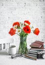 Bouquet of poppies, daisies, stack of books, cup of tea, camera on a table in a bright room. Cozy interior concept