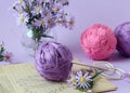 Bouquet of purple chrysanthemums with skeins of multicolored yarn, patterns and knitting needles, pastel background, side view